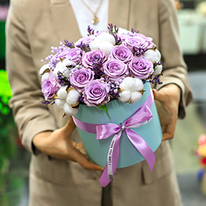 Композиция в шляпной коробке из лиловых роз Меритим, гипсофил и хлопка в Орехово-Зуево